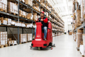 Warehouse Deep Cleaning, man operating ride-on scrubber dryer in a warehouse.