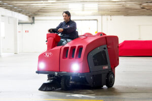 A man operating a industrial ride-on floor sweeper machine.