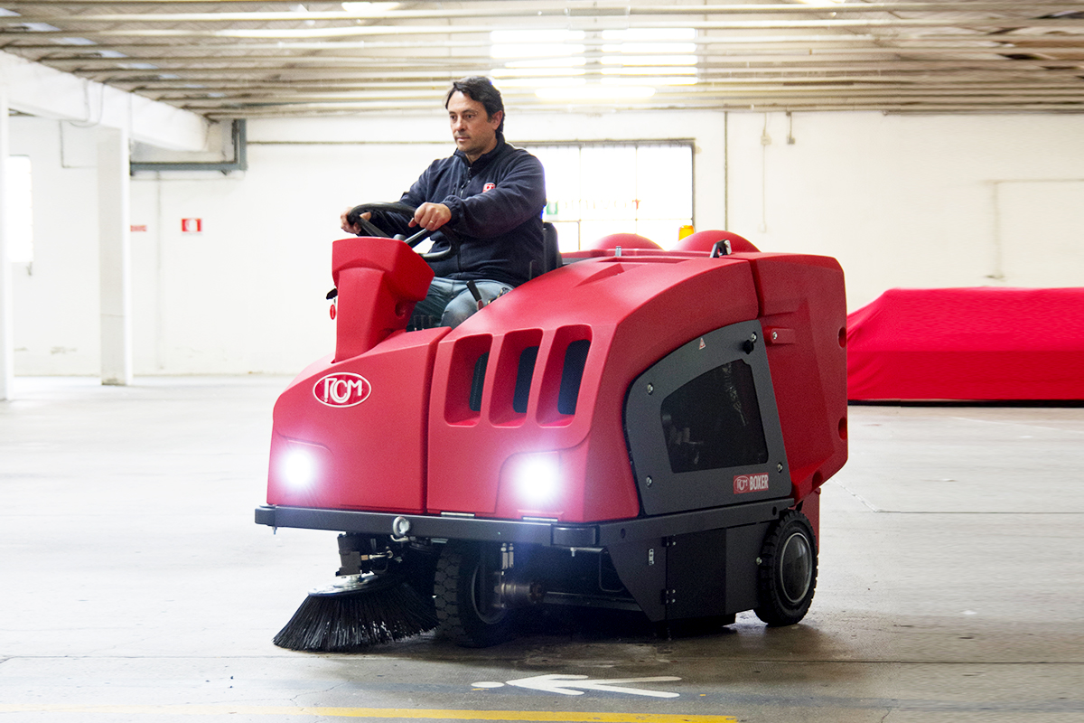 A man operating a industrial ride-on floor sweeper machine.